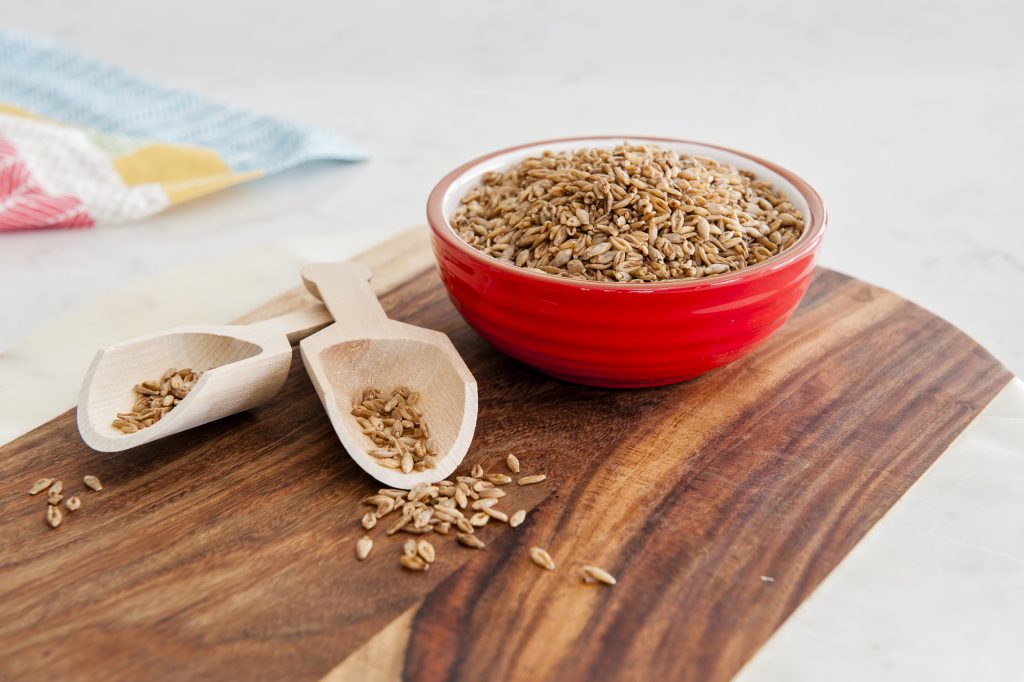 A bowl of BARLEYMAX® wholegrain barley steel cut whole grain on a wooden board with two wooden serving scoops.