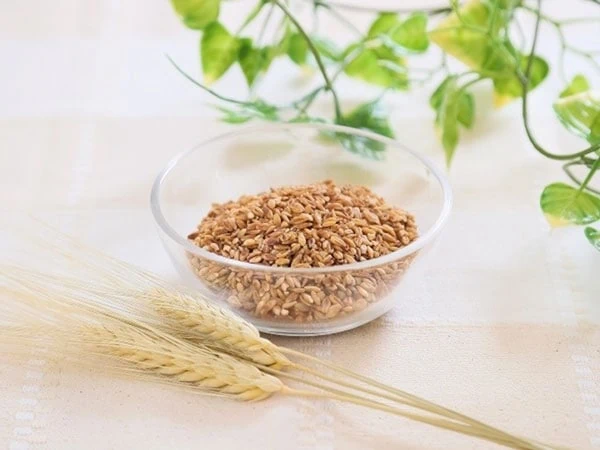 Barley flakes in a clear bowl with barley husks resting beside it